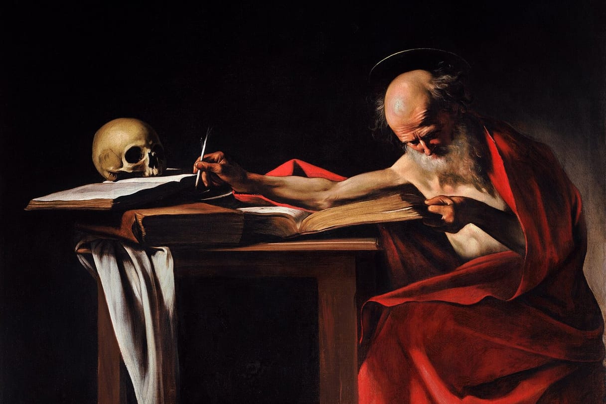 An elderly bald man in a red cloak leans over a table of books, stretching his pen toward an inkwell beside a skull.