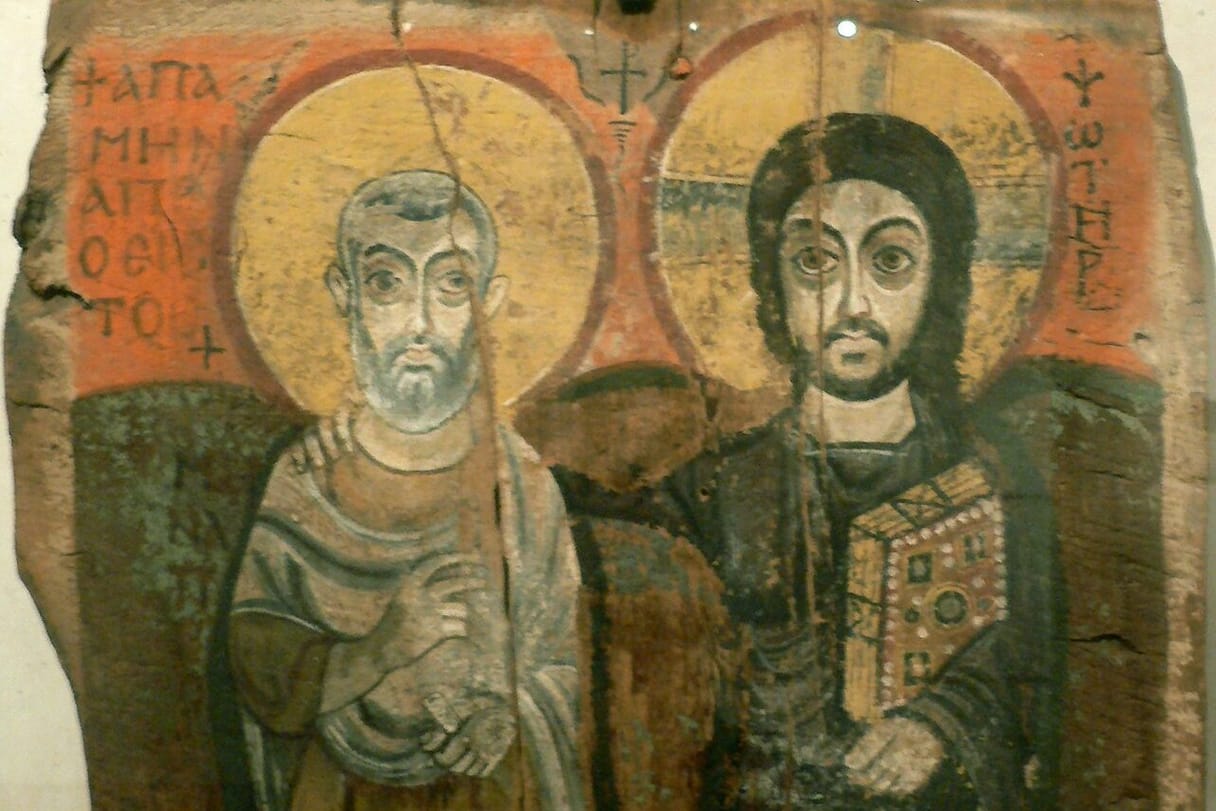 On a cracked wooden panel, Christ, holding a jeweled Gospel book, rests his arm on the shoulder of a gray-bearded abbot who stands beside him; both have large golden halos and wide, steady eyes.