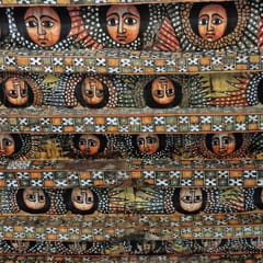 Rows of painted angel faces with large dark eyes and outspread wings fill the beams of a church ceiling, separated by bands of patterned crosses.