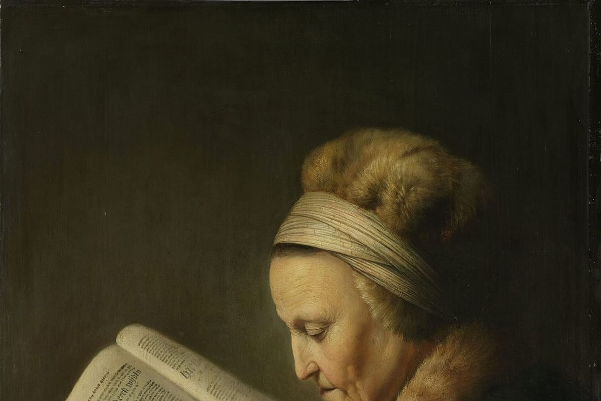 An elderly woman in a fur-trimmed hood bends close over a large open Bible, reading carefully.
