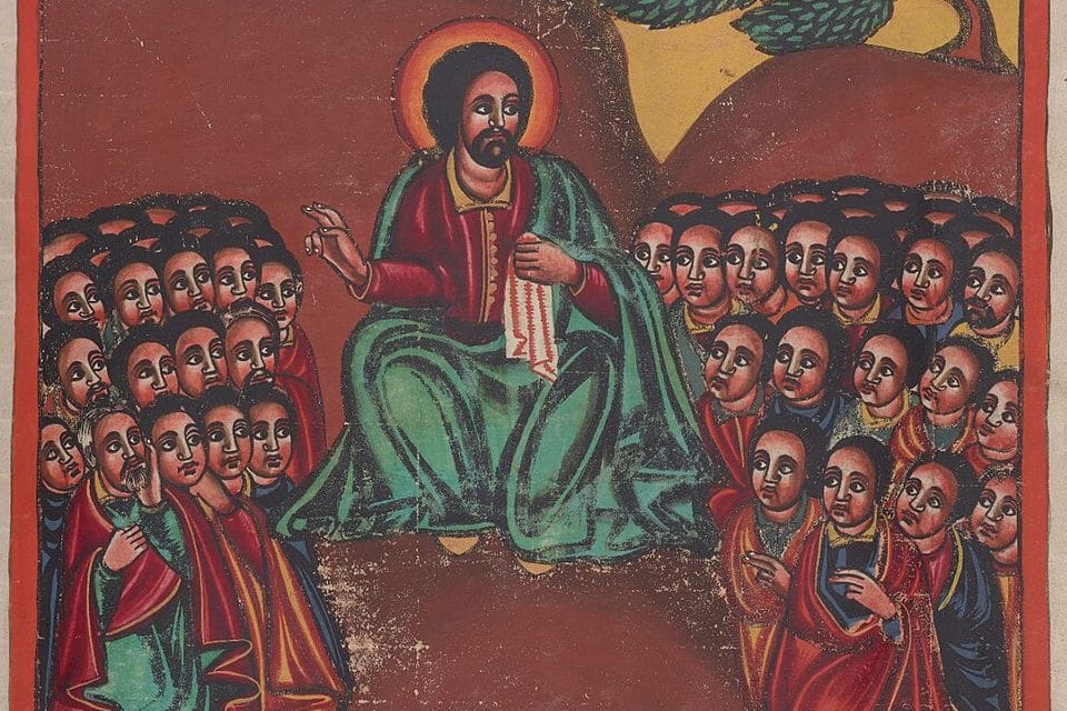Christ, with a red halo and a green mantle, sits on a hillside and raises one hand as he teaches, while crowds of listeners gather close on either side.