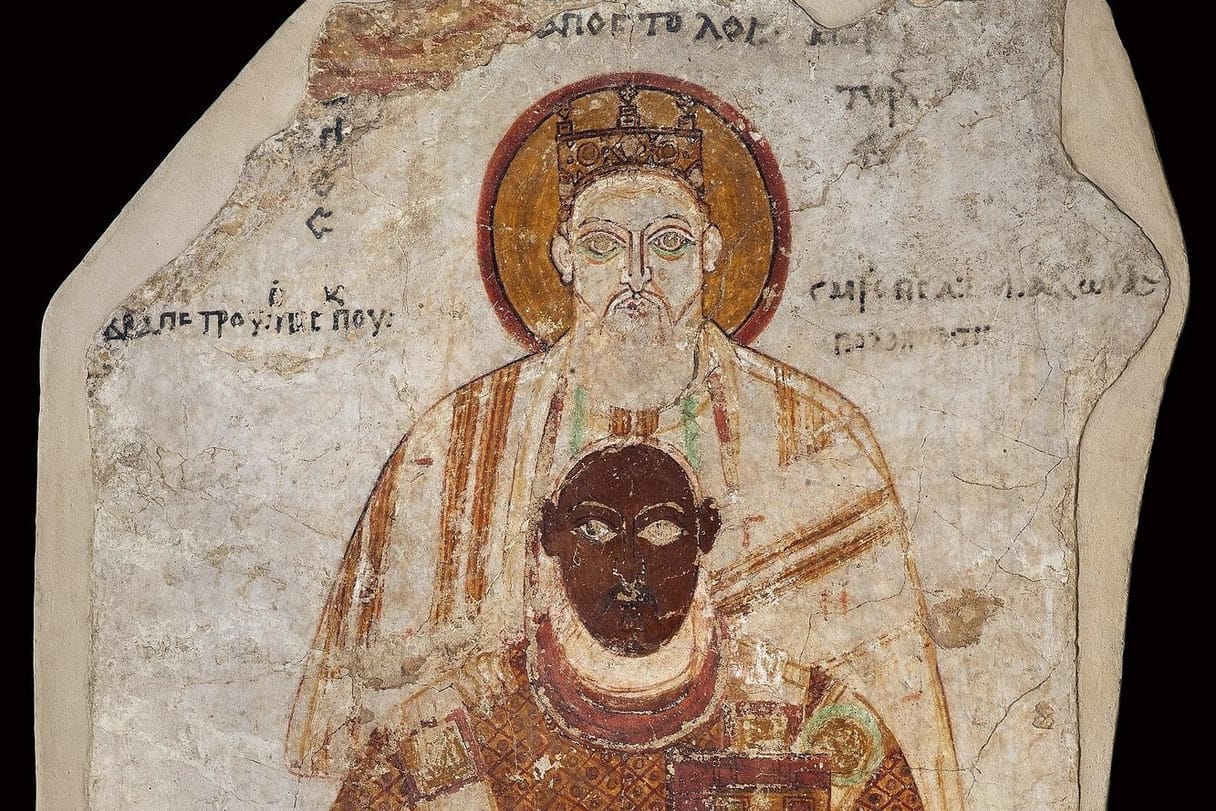 A wall painting of a dark-skinned Nubian bishop in a patterned red-brown vestment, holding a jeweled book, with the haloed apostle Peter standing close behind him and Greek inscriptions beside their heads.