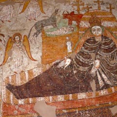 Mary, in a dark brown robe, reclines on a large patterned couch while the swaddled Christ Child lies in a manger above her, watched by an ox and a donkey; angels stand at the sides and the Magi ride in on horseback at the left.