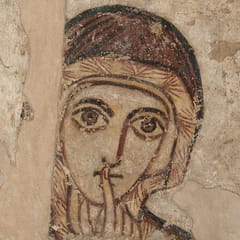A wall painting of a woman's face framed by a dark veil, with large, wide-open eyes and one finger raised to her lips; a Greek inscription runs down the left side.