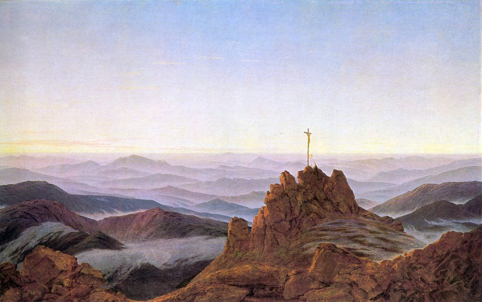 Morning light spreads over range after range of misty blue mountains, with a small cross standing on a rocky summit in the foreground.