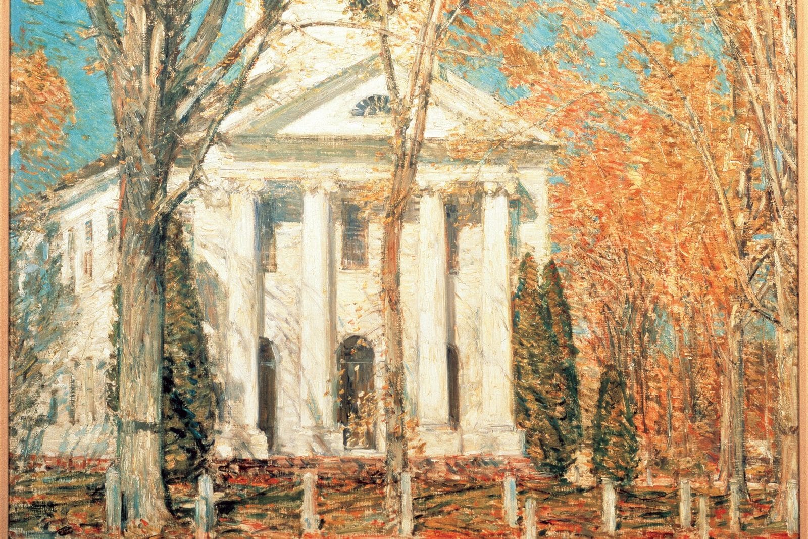 A white New England church with a columned portico stands among autumn trees with orange leaves under a blue sky.