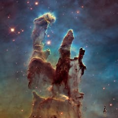 Towering columns of dark gas and dust, edged with light, rise against a blue field of stars in a region where new stars are forming.