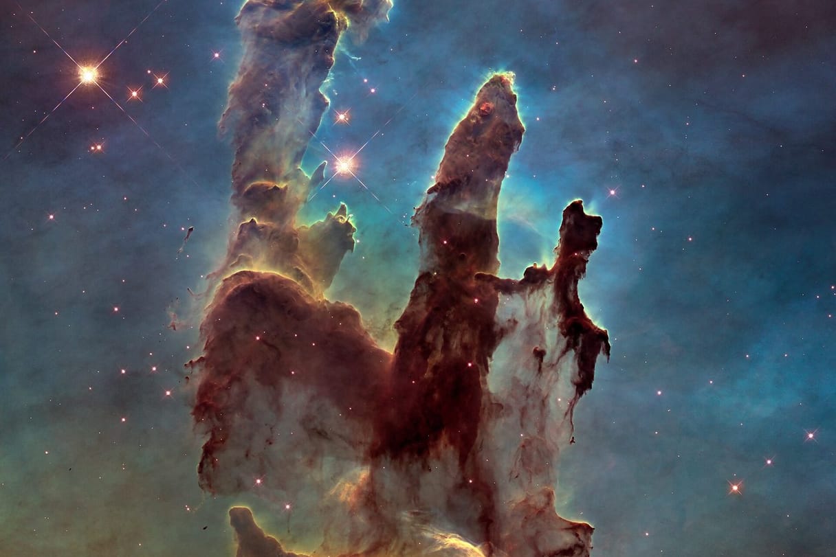 Towering columns of dark gas and dust, edged with light, rise against a blue field of stars in a region where new stars are forming.