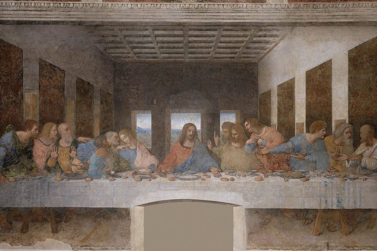 Jesus sits at the center of a long table with bread and wine, the twelve apostles gathered in agitated groups on either side of him.