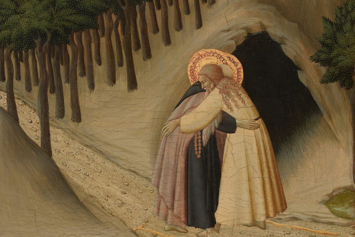 Two old haloed hermits embrace on a pale desert path before a dark cave, one in a black habit and pink cloak with a string of red prayer beads, the other with long flowing hair in a pale robe, beneath a row of dark trees.