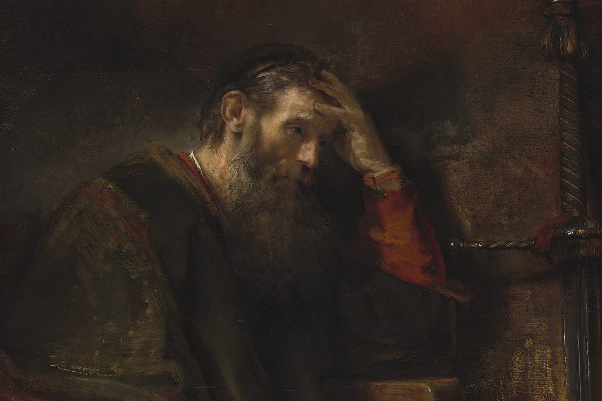 An older bearded man in a dark robe sits at his desk, resting his head on his hand in thought.