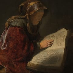 An old woman in a fur-trimmed red cloak and a gold headscarf reads a large open book, her hand resting on the page.