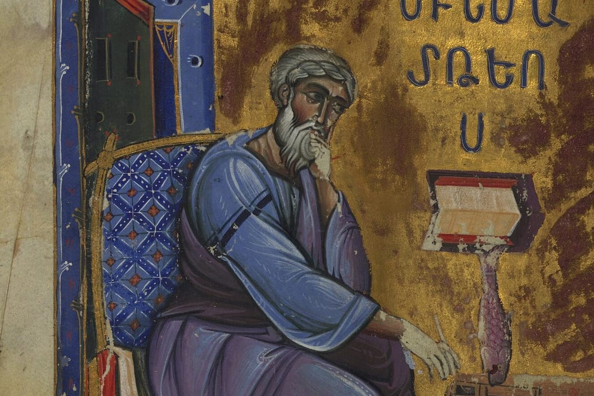 A gray-bearded evangelist in a blue robe sits in a cushioned chair with his hand at his chin in thought, before a lectern holding an open book, under his name in Armenian letters on a gold ground.
