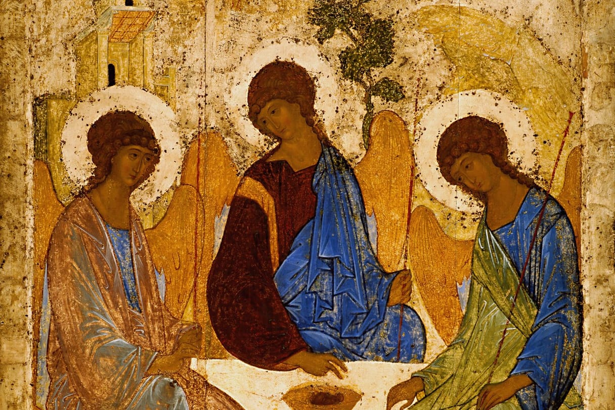 Three haloed angels with golden wings sit around a table bearing a single cup, their heads inclined toward one another.