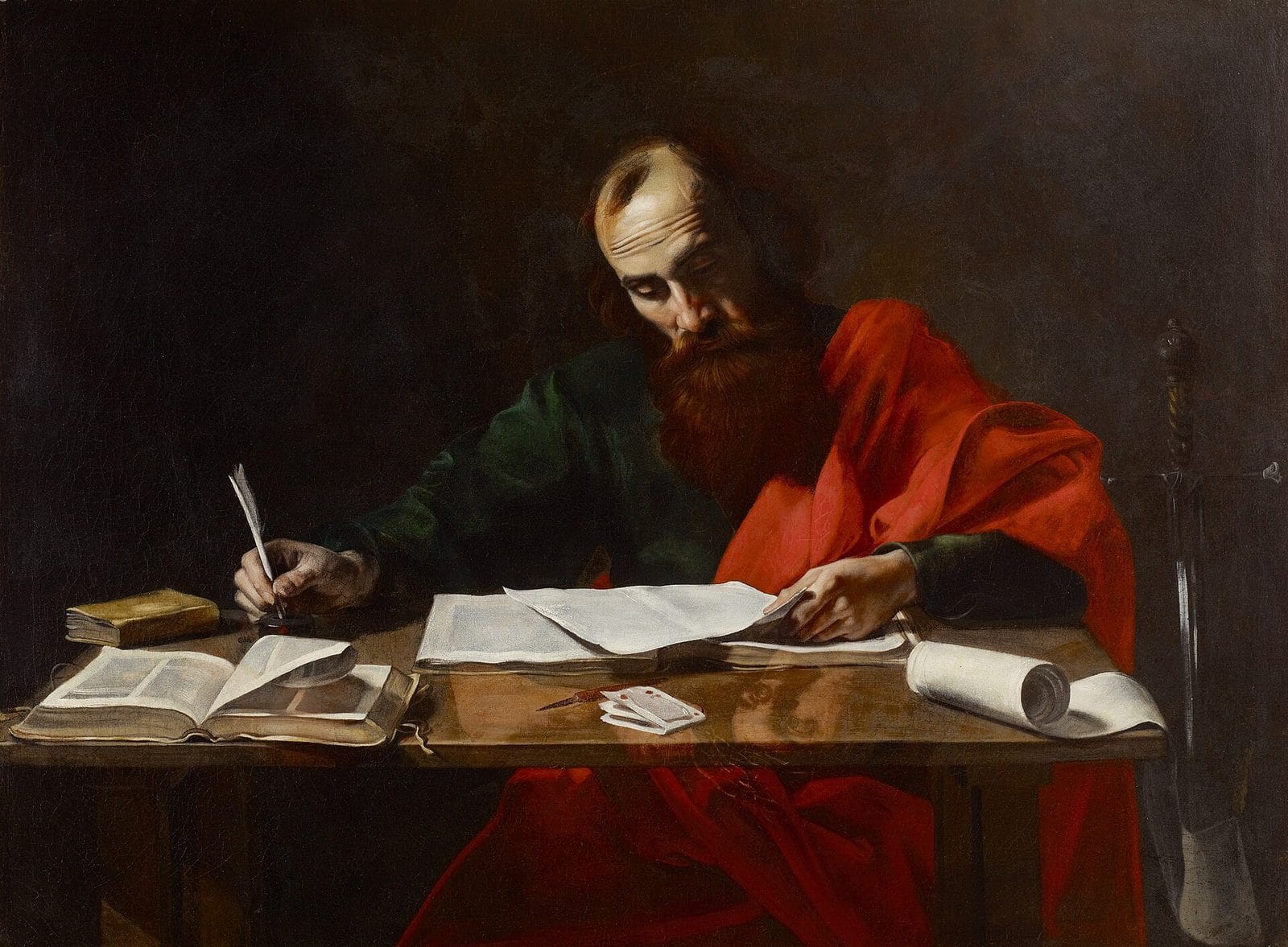 The apostle Paul, in a red cloak, sits at a table covered with books and papers, writing a letter with a quill.