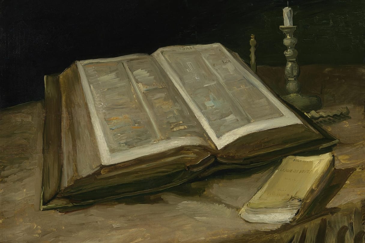 A large open Bible lies on a dark tablecloth beside a snuffed candle and a small, worn yellow paperback.
