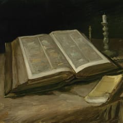 A large open Bible lies on a dark tablecloth beside a snuffed candle and a small, worn yellow paperback.