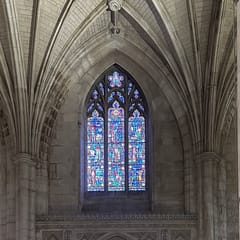 Pale stone columns and ribbed Gothic vaults frame a tall stained-glass window in a quiet bay of the cathedral.